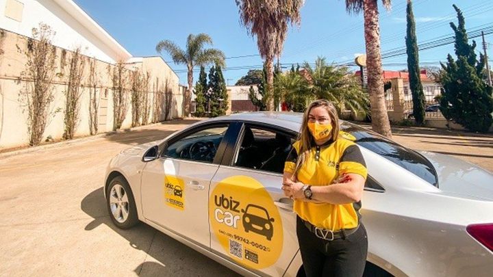 A motorista pousando ao lado de seu carro adesivado com a marca da Ubiz Car
