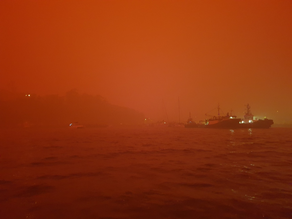 Orange smoke haze across water, from bushfires
