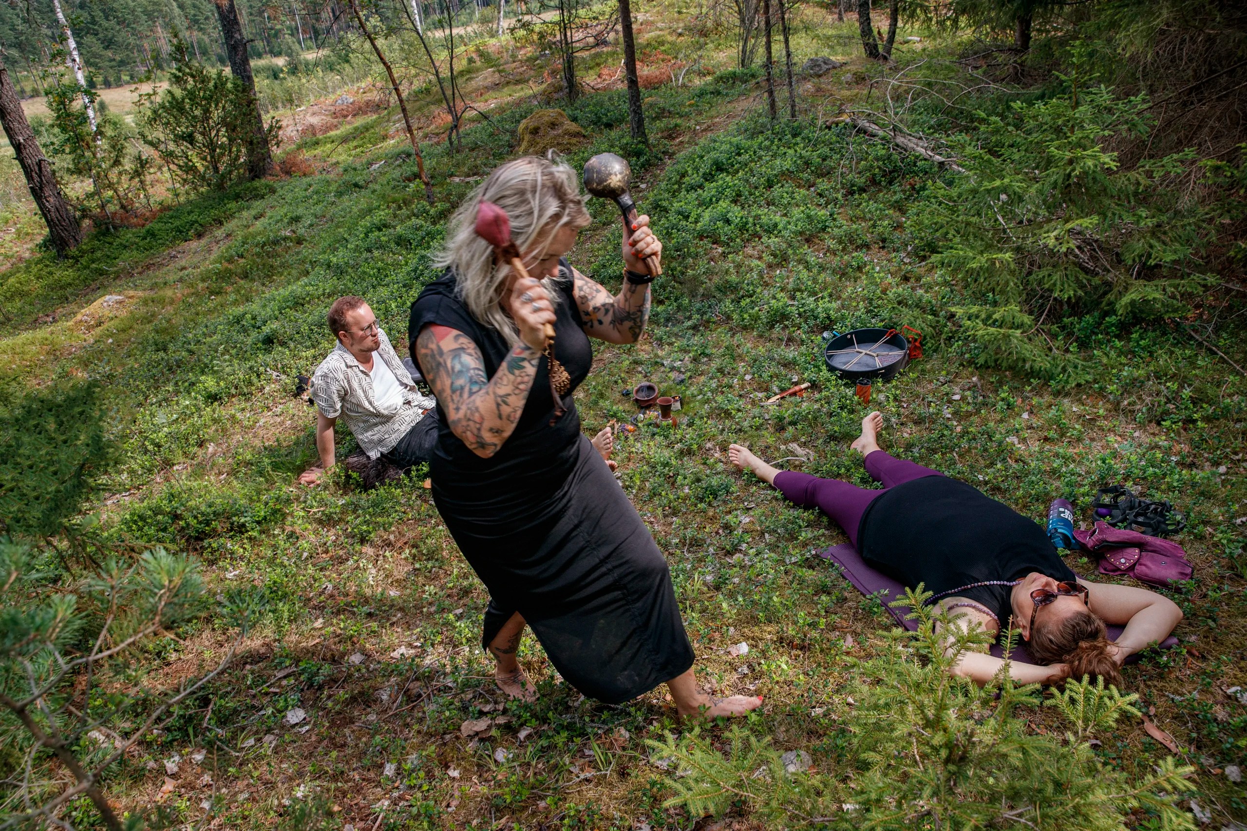 Häxan Rebecca Tiger skakar maracas, Jonatan och Laurie ligger på marken i skogen.