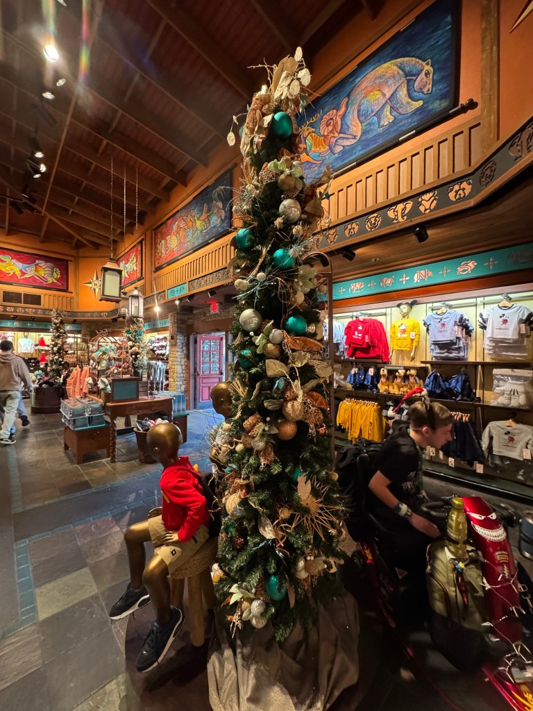 A decorated holiday tree with teal and gold ornaments inside a store at Animal Kingdom, showcasing festive decor amidst merchandise displays.