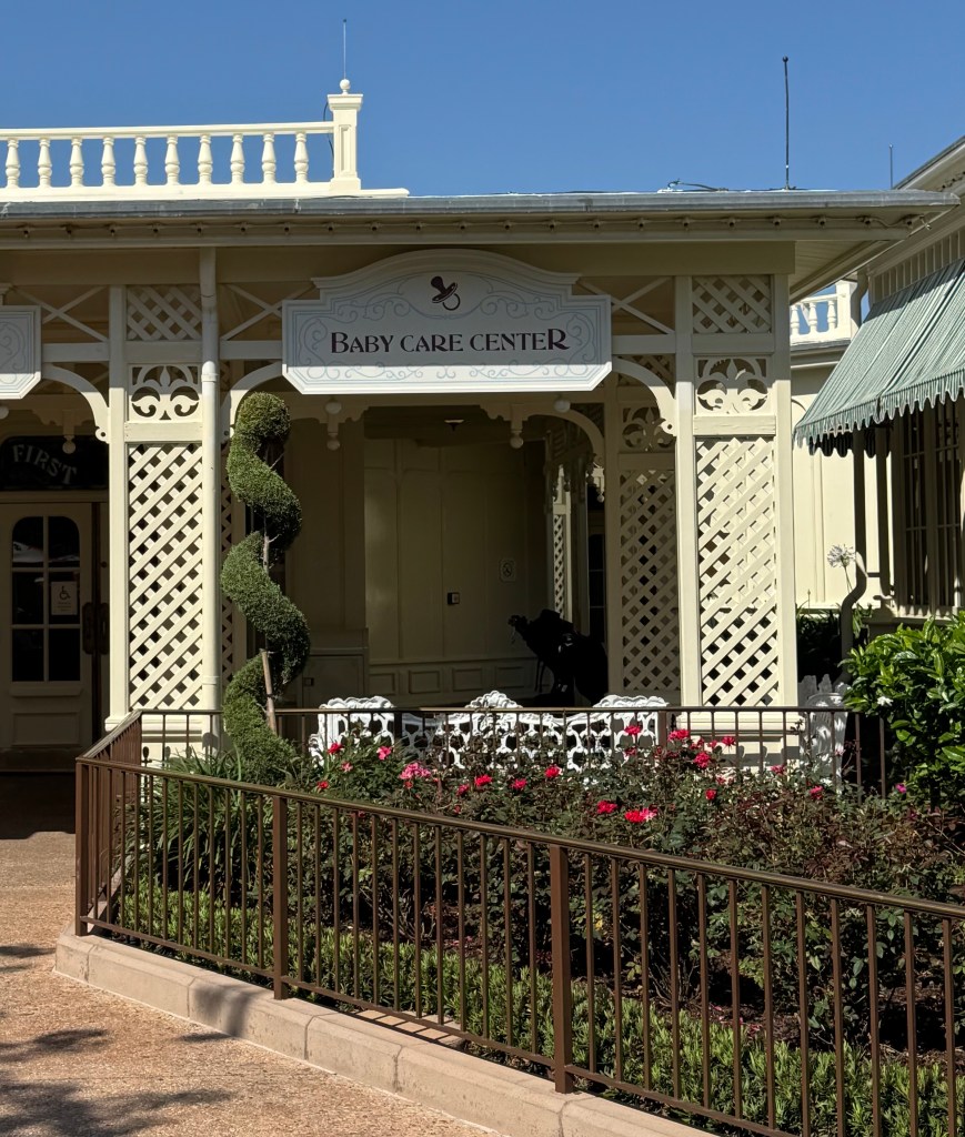Entrance of the Baby Care Center at Walt Disney World, featuring a decorative sign and landscaped flower beds.