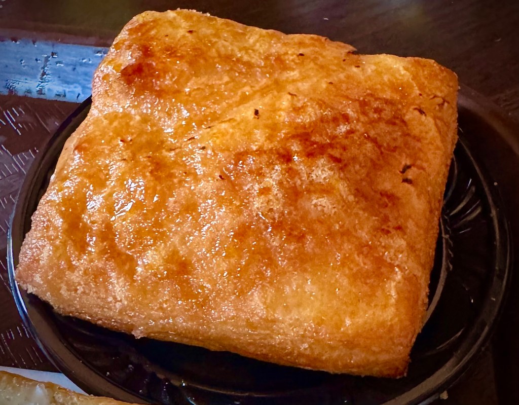 A warm, flaky Ham and Gruyere Tart served on a black plate, showcasing a golden, crispy exterior.