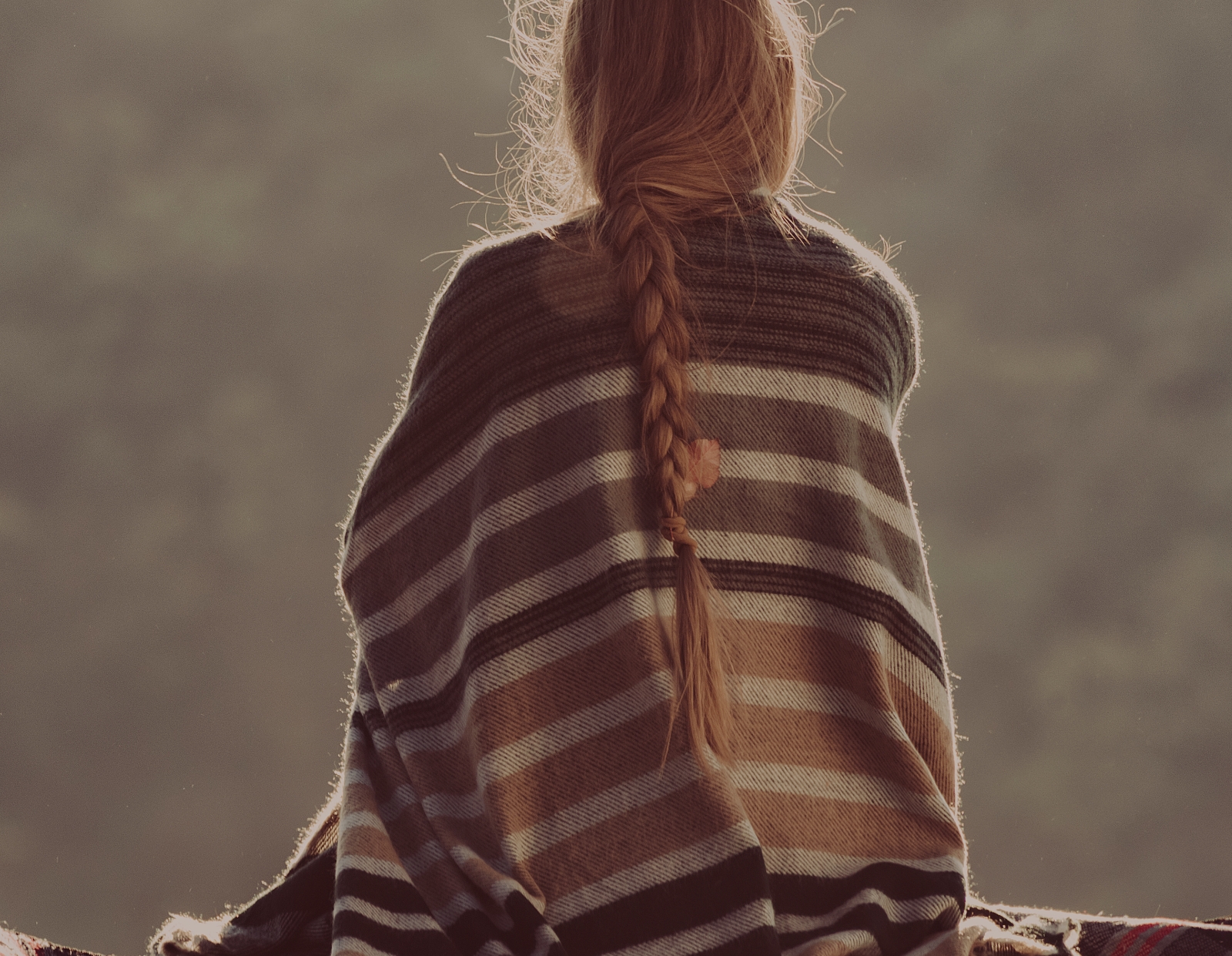 A person sits wrapped in a blanket, looking out quietly, reflecting during a moment of pause and introspection.