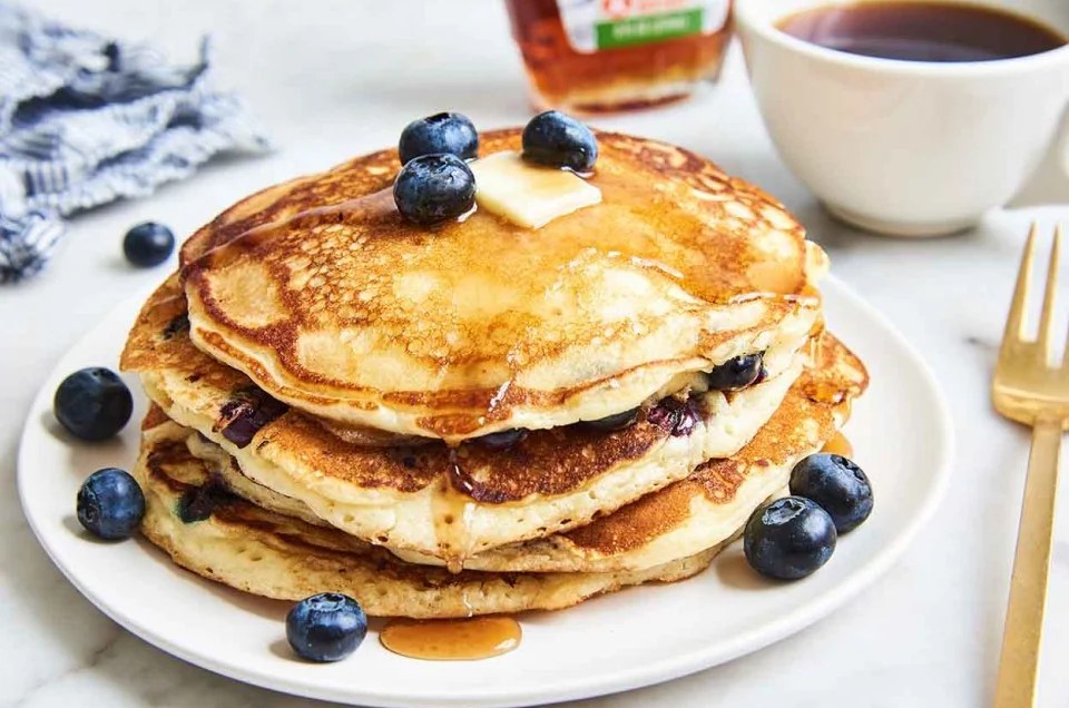 Blueberry pancakes on a plate with a cup of coffee and a bottle of maple syrup