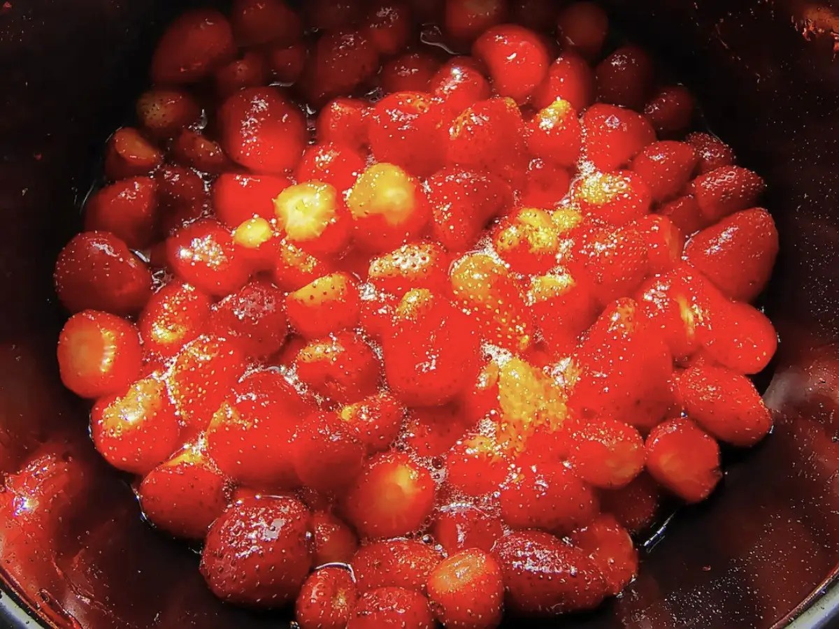 Whole strawberries added to hot sugar syrup in a wide pot while making Romanian strawberry preserve.