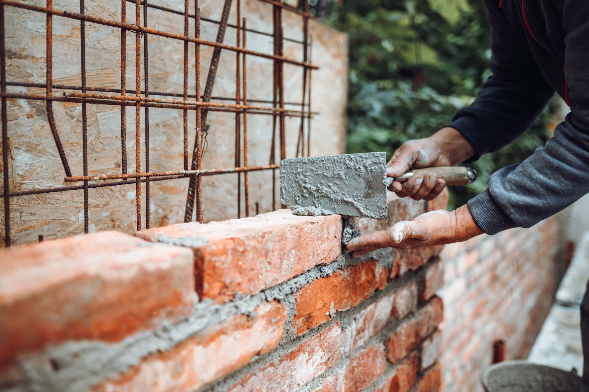 Professional worker using pan knife for building brick walls with cement and mortar