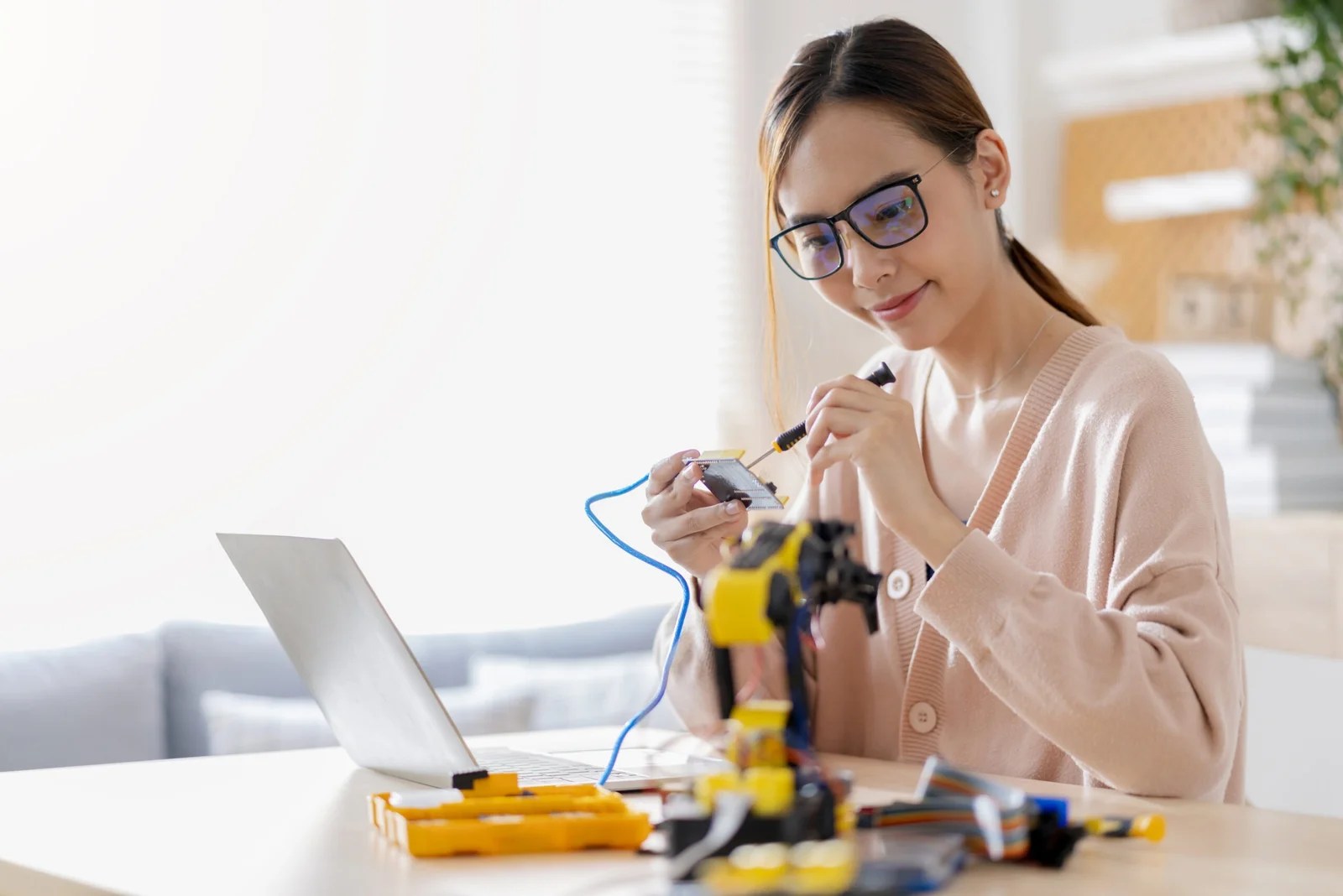 smart asian female programer learning robot arm ai coding electronic board cable in STEM, STEAM she try to testing her autonomous  robotic arm with sensors via Arduino platform at home