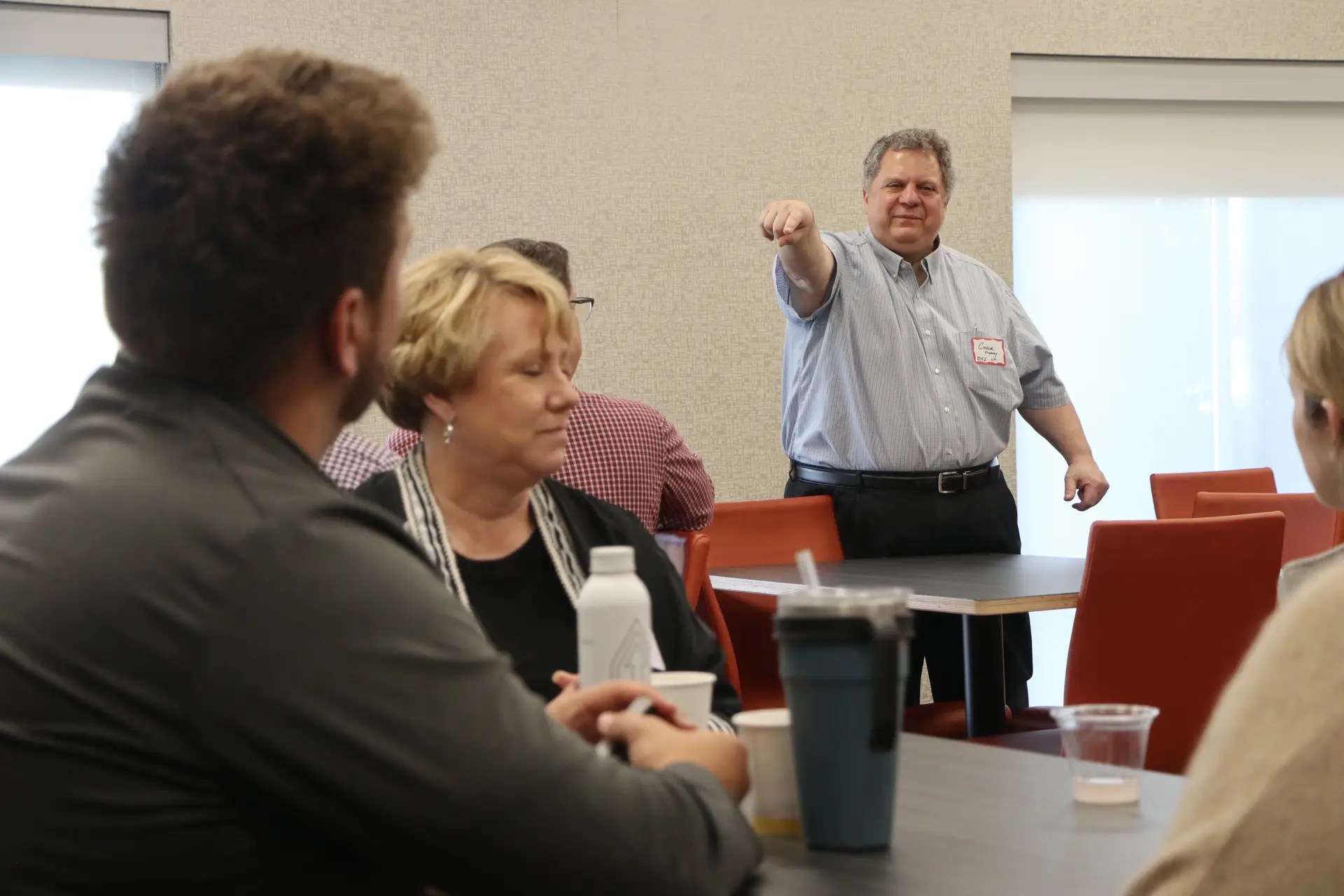 Facilitator standing and pointing during a meeting with seated colleagues around a conference table.