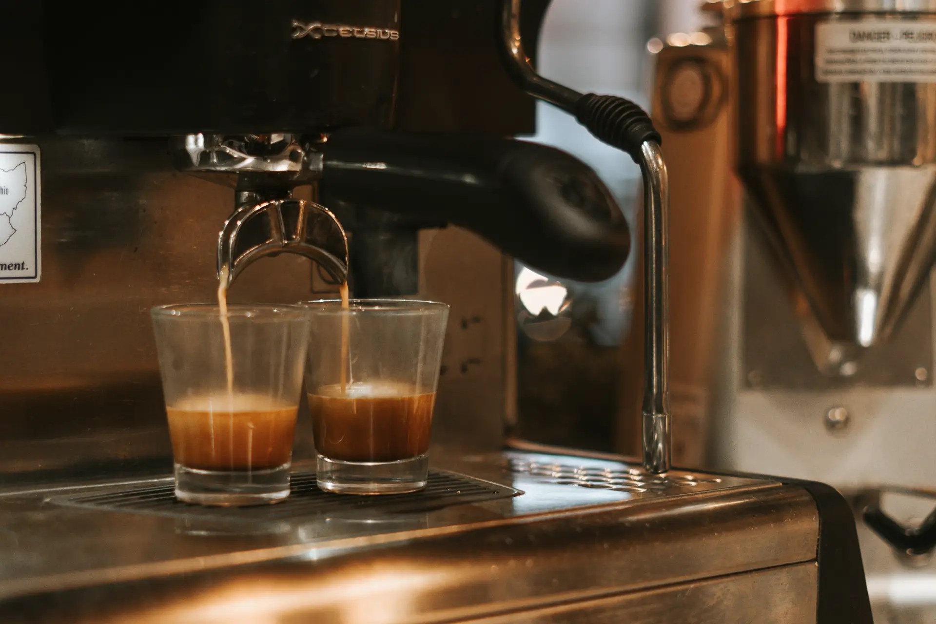 Espresso machine pouring two shots of espresso into small glass cups on a metal counter.