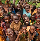 Group of smiling children gathered outdoors, posing for the camera in a sunny rural setting.
