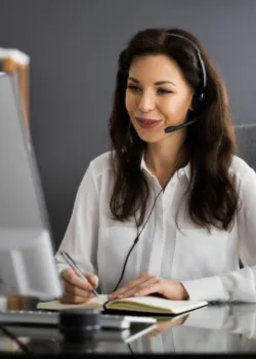 woman smiling at computer screen with notebook and headphones on