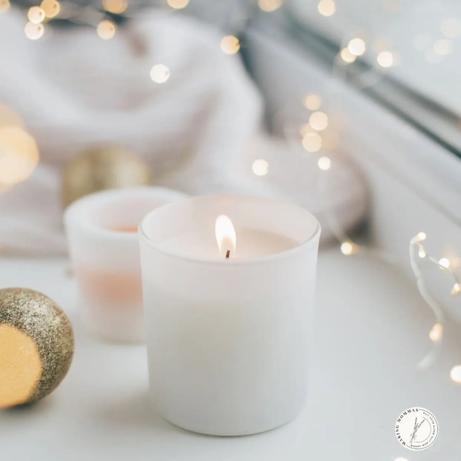 White candle glowing softly on a windowsill surrounded by warm fairy lights and golden Christmas ornaments, creating a cozy and peaceful holiday atmosphere for a home office.