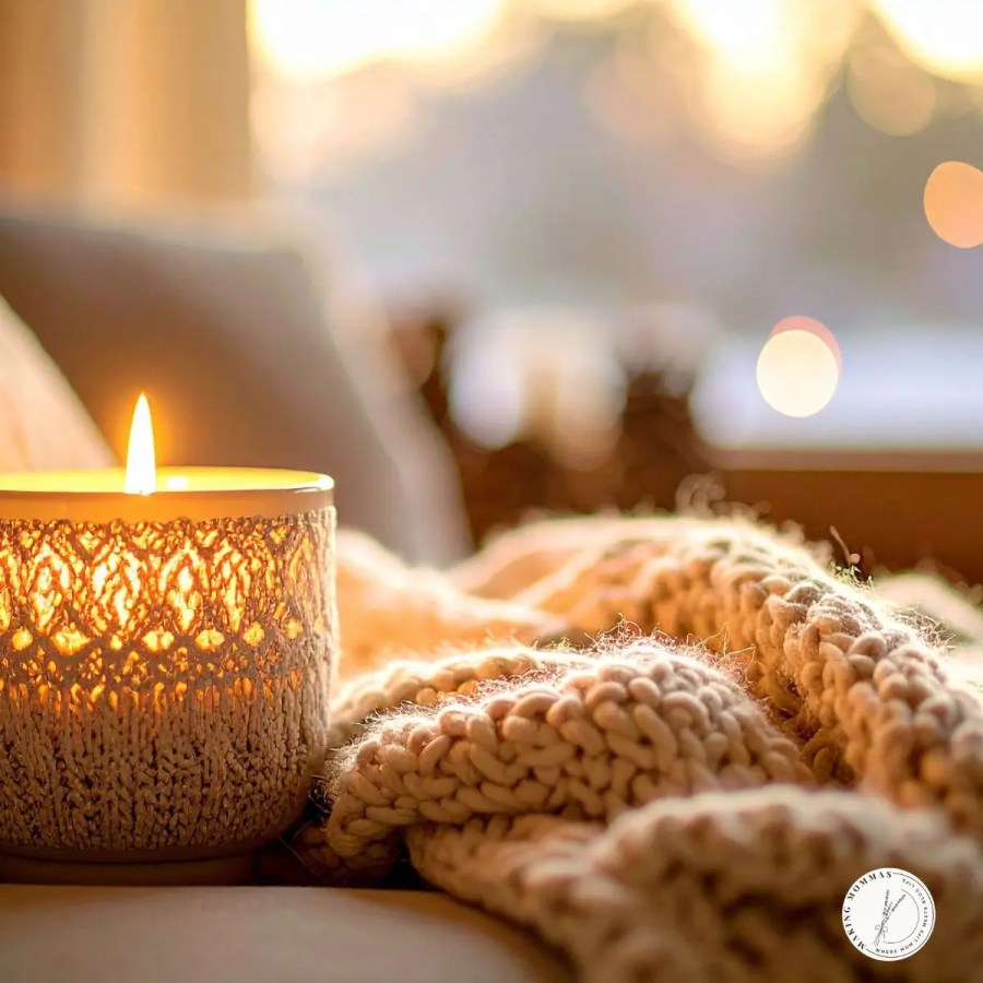Lit candle in a cozy knitted holder beside a soft blanket — a warm and inviting Christmas gift idea for stay-at-home moms who love relaxing winter evenings.