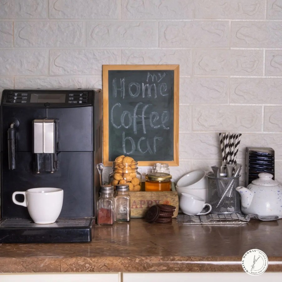 Cozy home coffee bar setup with an espresso machine, mugs, cookies, and jars of ingredients on a countertop beside a chalkboard sign that reads “my home coffee bar,” creating a warm, inviting workspace atmosphere.