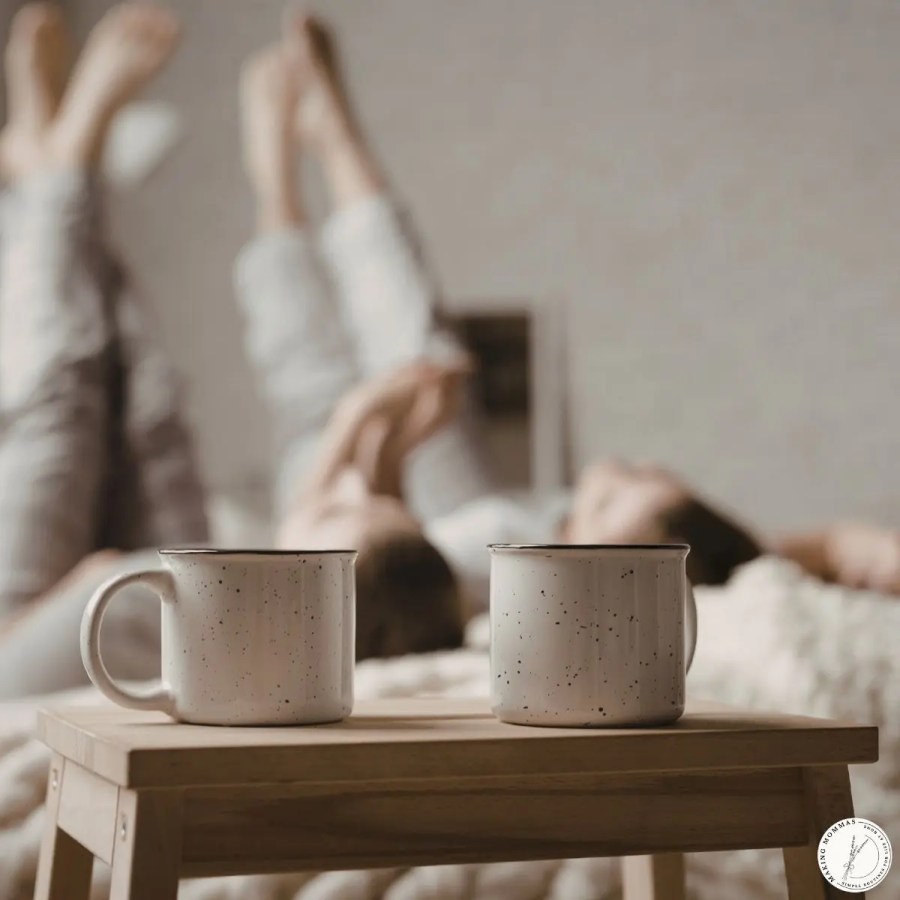 Two mugs on a small table in a bedroom, with a family relaxing in the background, representing a calm daily flow and unhurried moments at home.