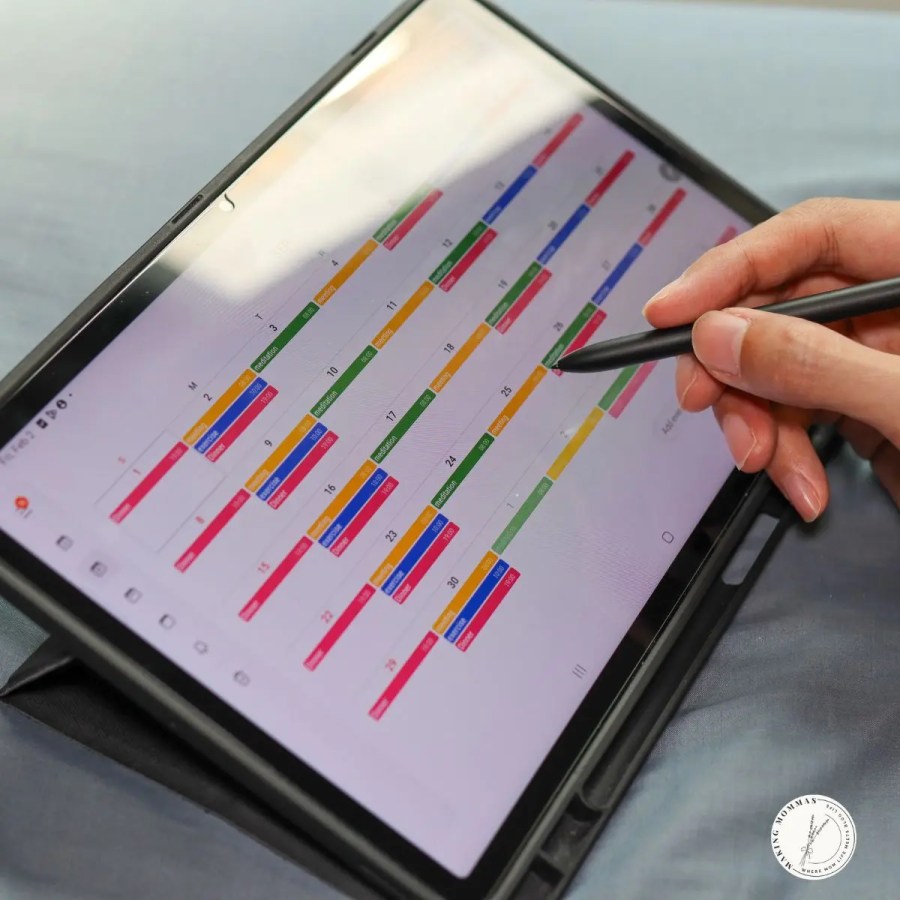 A person using a stylus to organize a colorful digital calendar on a tablet screen.
