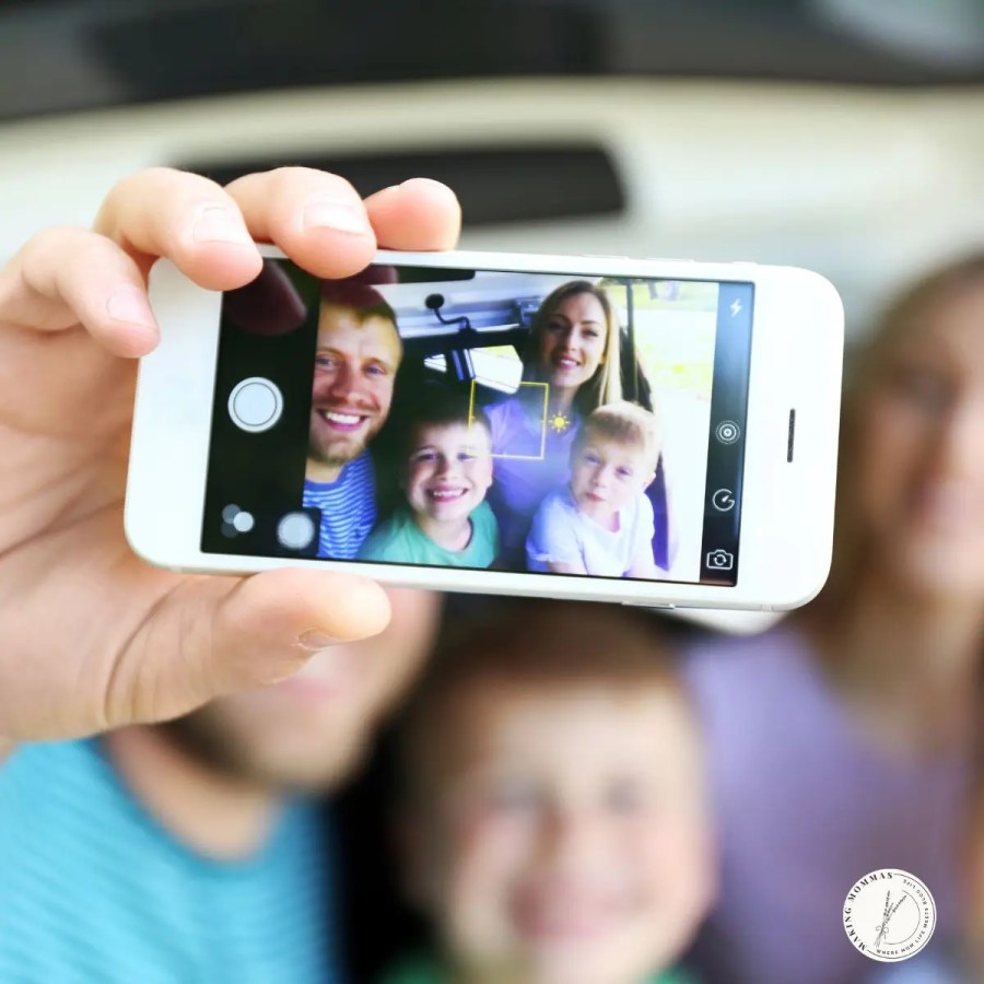 A family taking a selfie together, shown on a smartphone screen with a man, woman, and two children smiling for the picture.