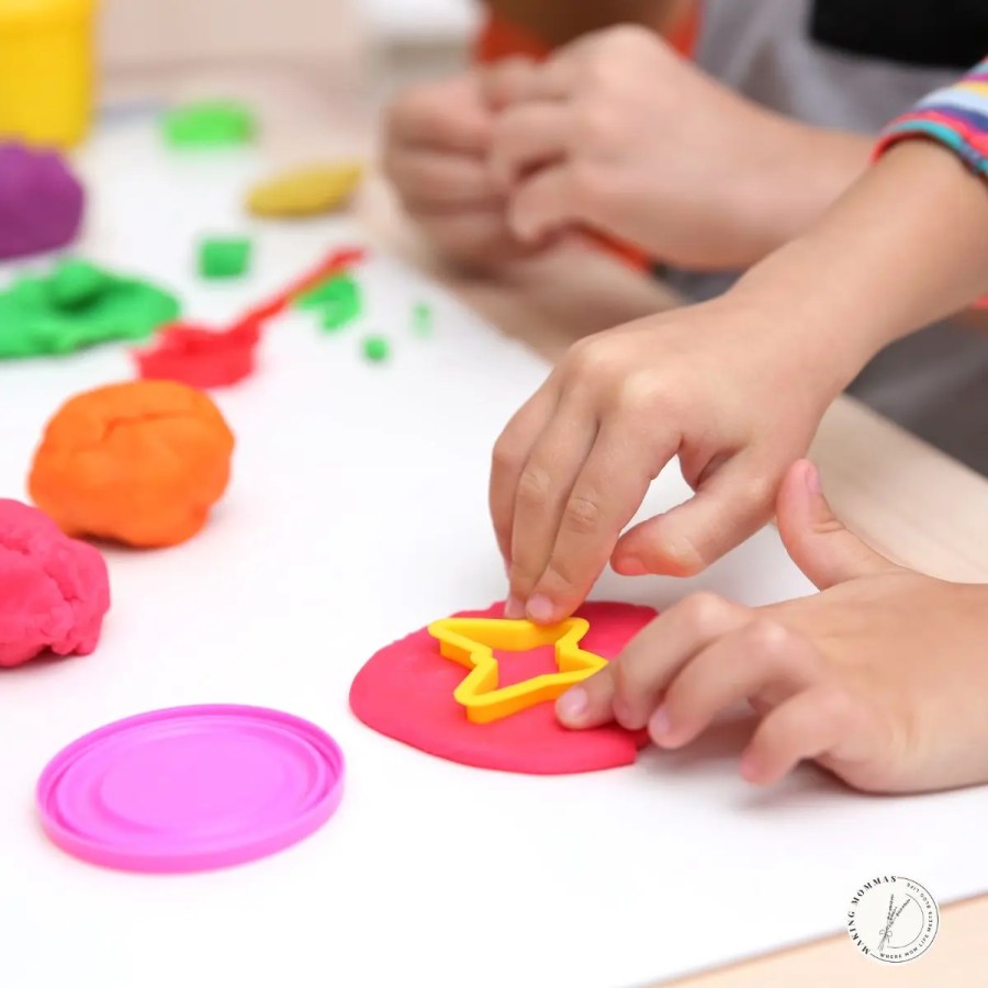Close-up of children playing with colorful playdough and using a yellow star-shaped cutter on a red piece of dough.