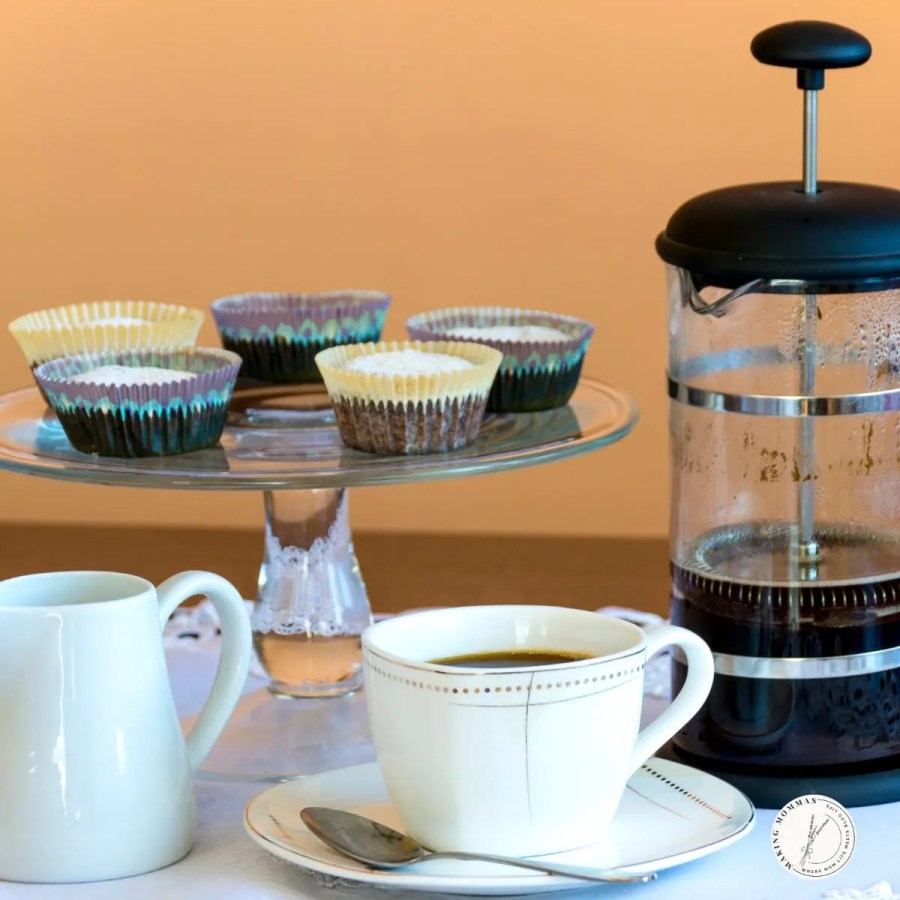 French press coffee maker beside a cup of freshly brewed coffee and homemade muffins, perfect for moms who enjoy a slow morning ritual with rich, flavorful coffee.