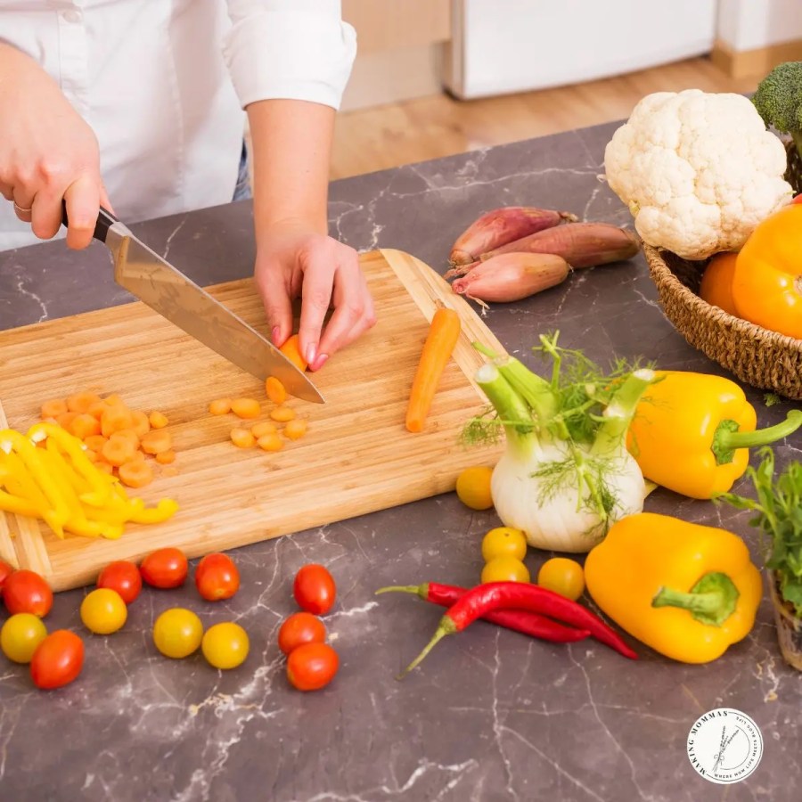 Close-up of a woman chopping fresh vegetables on a wooden cutting board with a sharp kitchen knife — a thoughtful and practical Christmas gift for stay-at-home moms who love to cook.
