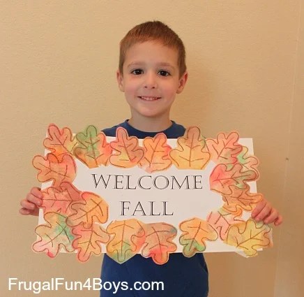 Child holding a handmade “Welcome Fall” sign decorated with colorful watercolor fall leaves.