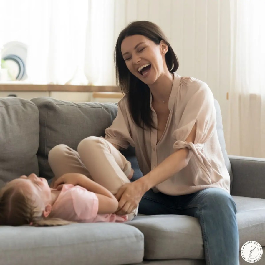 A stay-at-home mom laughing and playing with her young child on the couch, showing connection, presence, and limiting distractions at home.