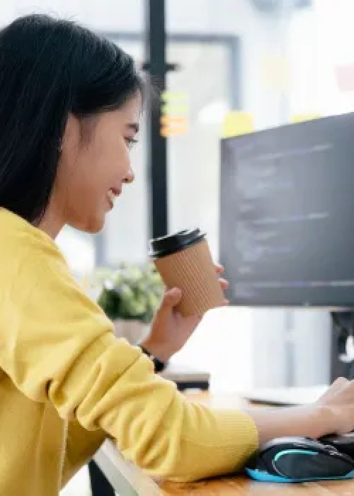 woman in yellow shirt with coffee smiling at computer screen