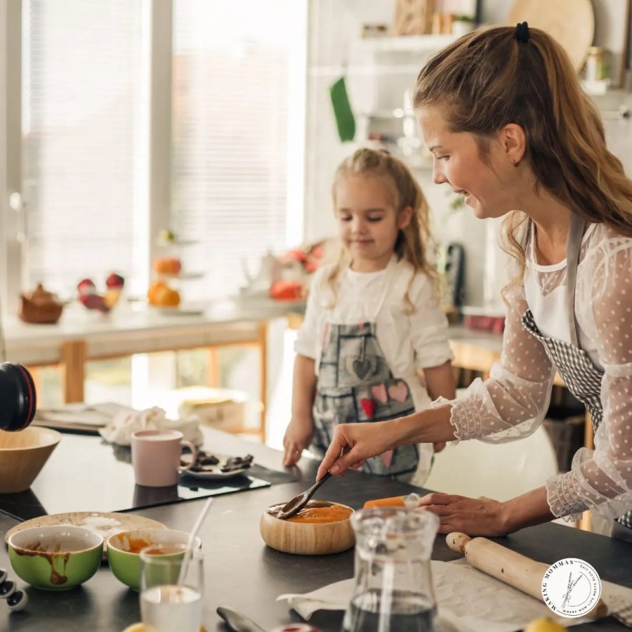 Smiling mom and daughter in aprons preparing food together in a bright kitchen.