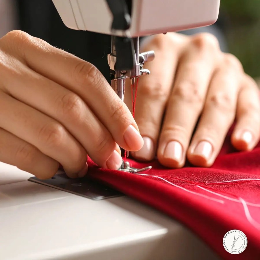 Close-up of a person using a sewing machine to stitch red fabric with red thread, showing careful hands guiding the material.