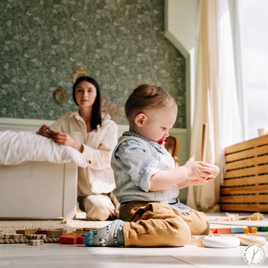 A toddler playing quietly with wooden toys on the floor while mom tidies nearby, showing the steady rhythm of everyday routines at home.