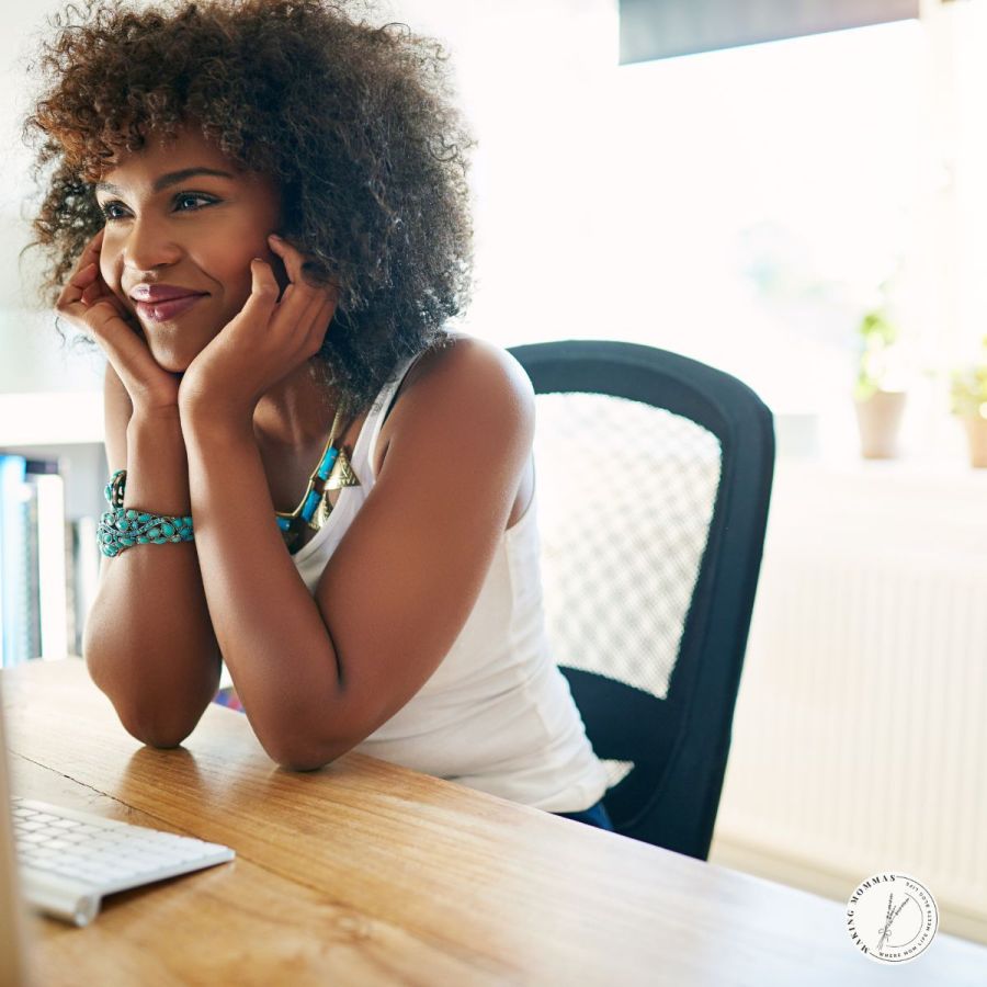 Smiling woman sitting at her desk in a bright, modern home office, looking inspired and focused while working on her computer — a moment that captures motivation and creativity in a productive workspace.