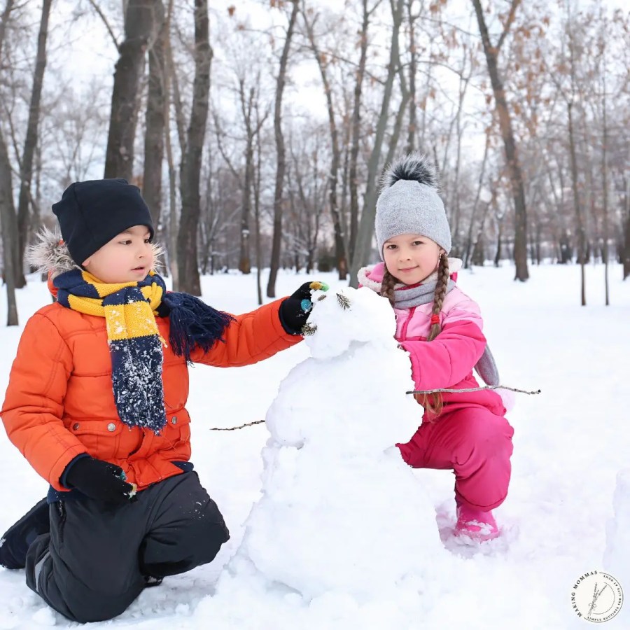 Two young children bundled in winter clothes building a snowman outdoors, showing simple winter activities for kids on snowy days.