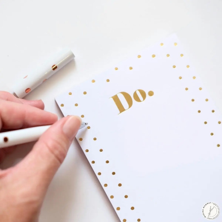 Hand writing a short to-do list on a simple notepad, representing choosing just a few daily priorities instead of an overwhelming task list.