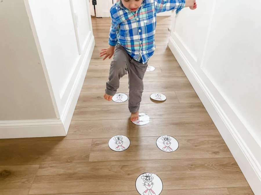 Toddler stepping on printable Easter bunny hop game circles placed on the floor, practicing balance and gross motor skills in a hallway.