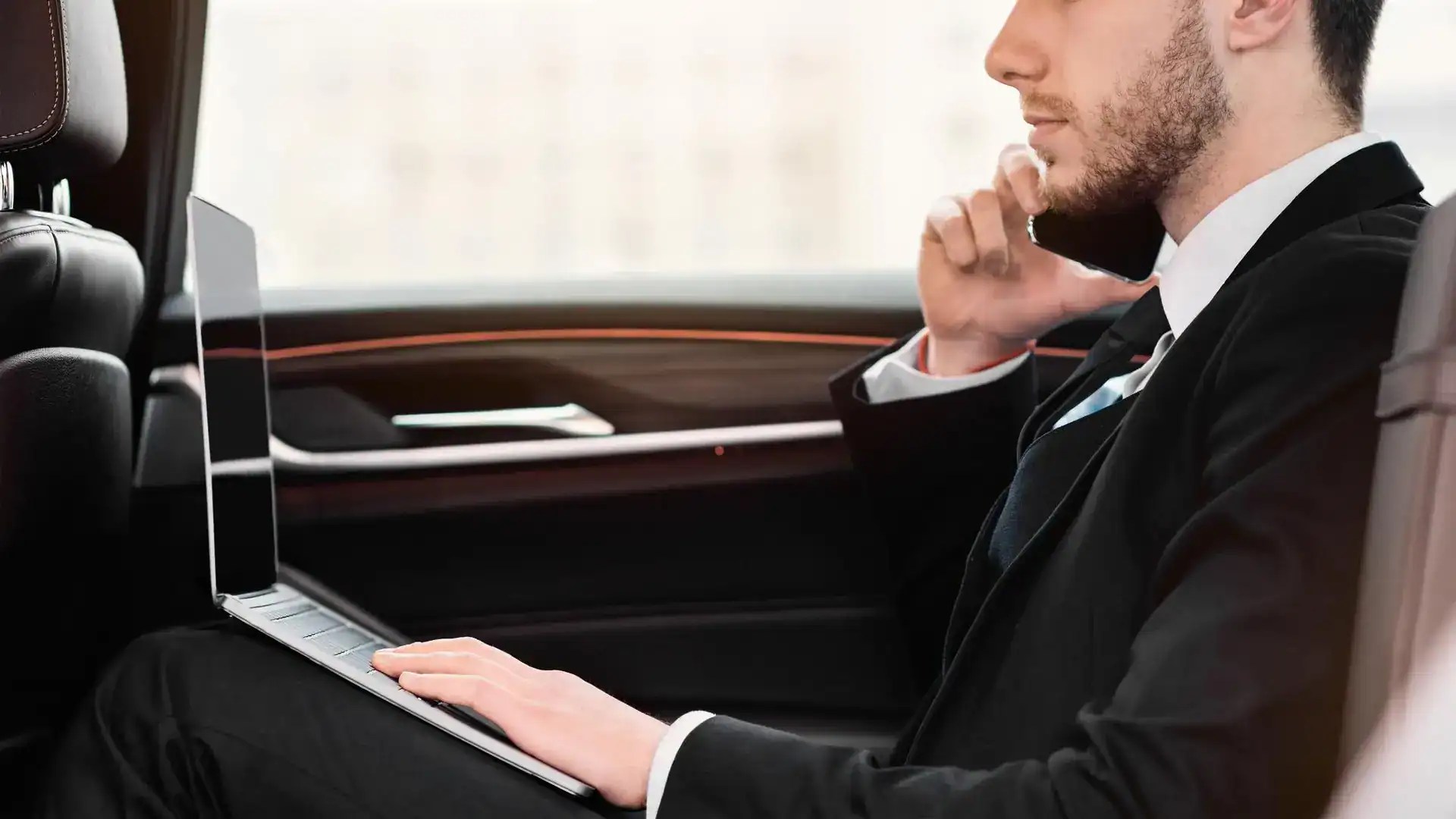 Man using a laptop in a luxury car, professional chauffeur service.