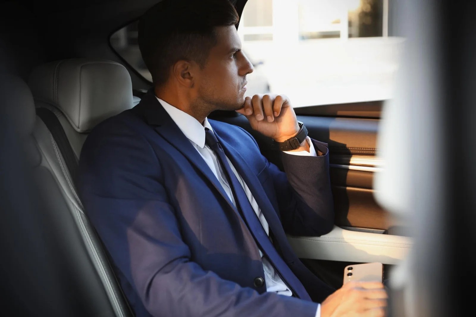 Man in suit sitting in luxury car, ready for chauffeur service.