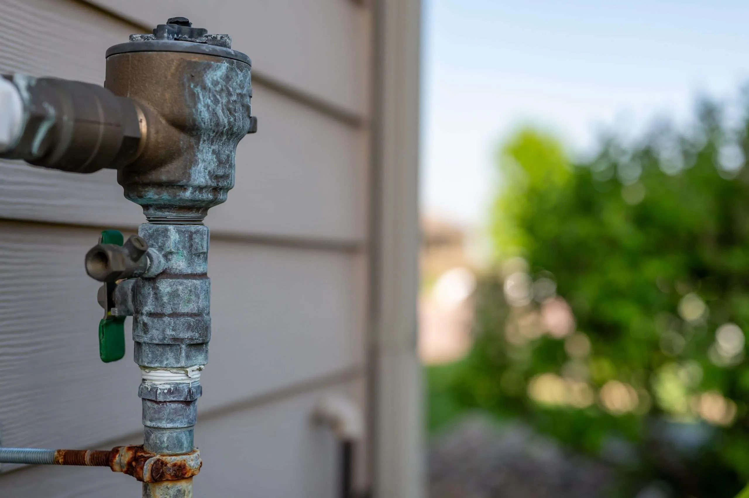 Rusted outdoor water sprinkler backflow preventer on the side of a residential house