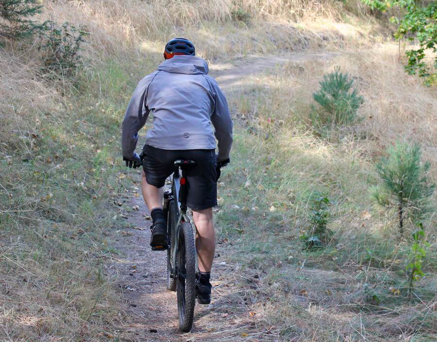 This photo shows the backside of the Showers Pass Elements mountain biking rain jacket on a gear tester riding a bike.