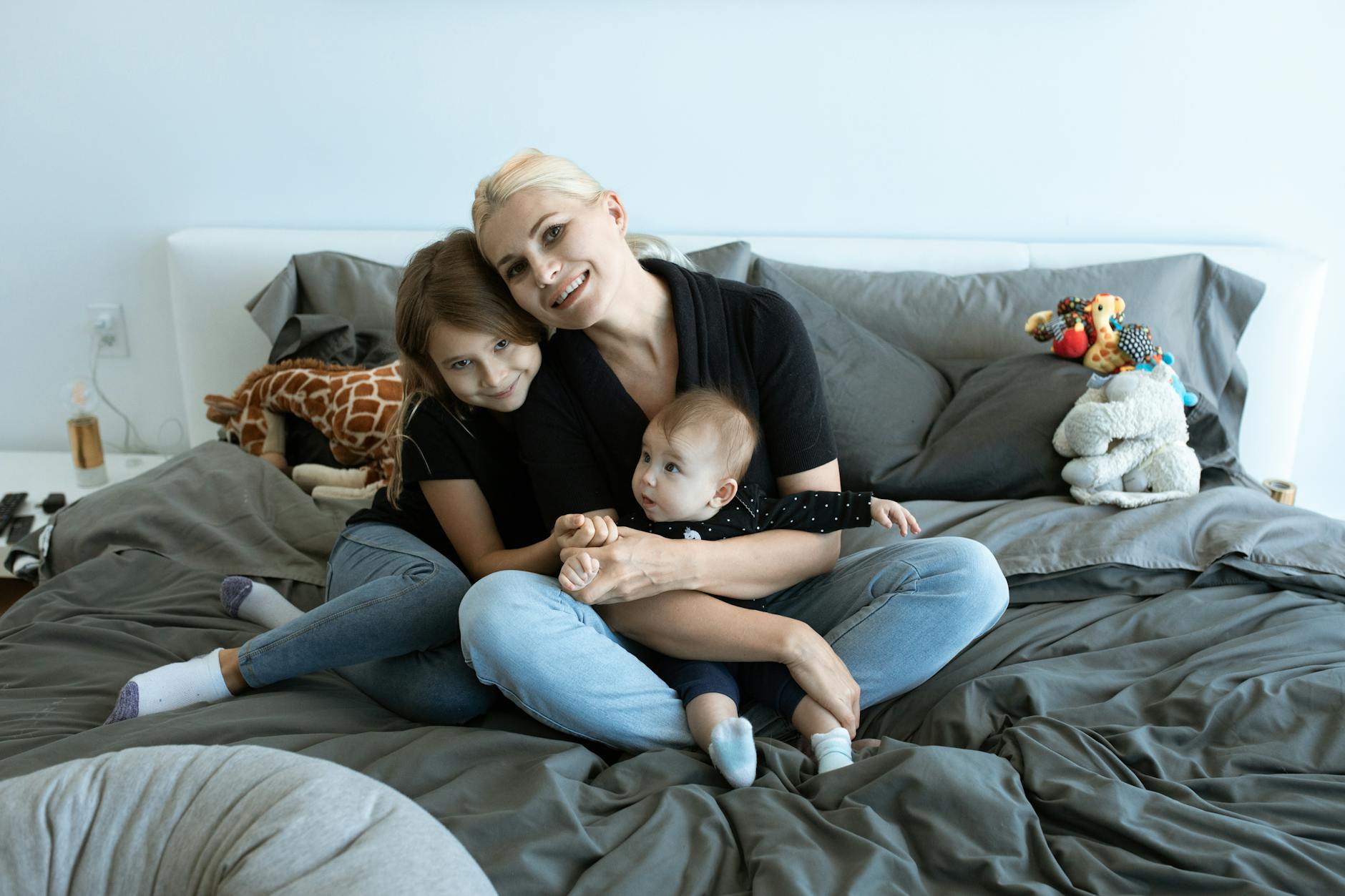 mother and daughters sitting on the bed while smiling at the camera