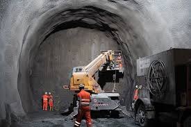 Heavy construction equipment operating inside a tunnel with workers present.