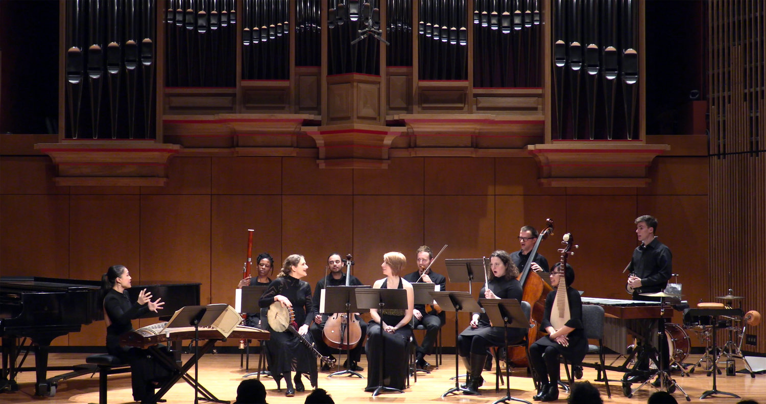 Ensemble of musicians seated beneath a massive pipe organ.