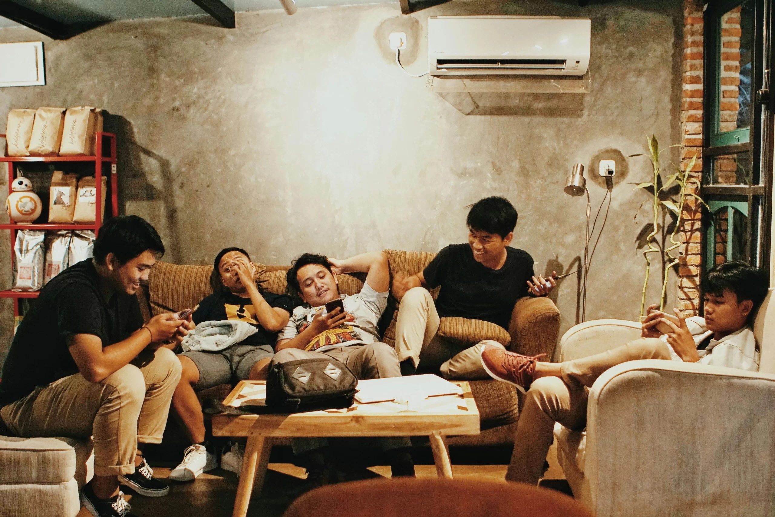 Group of friends relaxing on couches while browsing on their phones.