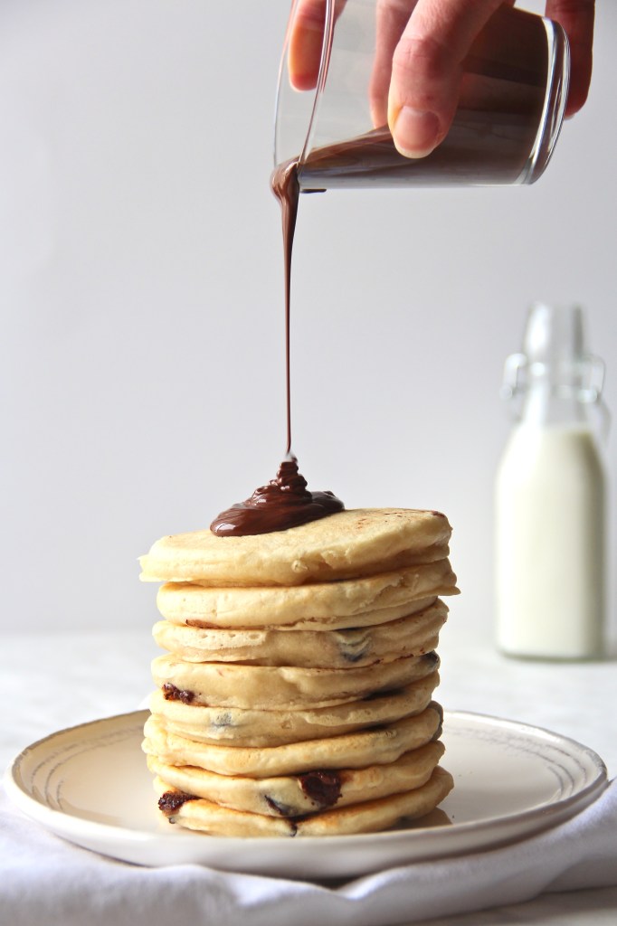 Chocolate sauce poured on coconut chocolate chip pancakes stacked in a plate