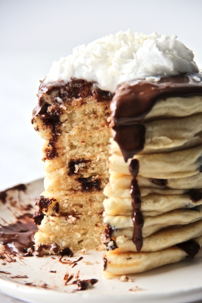 stack of coconut pancake with chocolate sauce and whipped cream in a plate