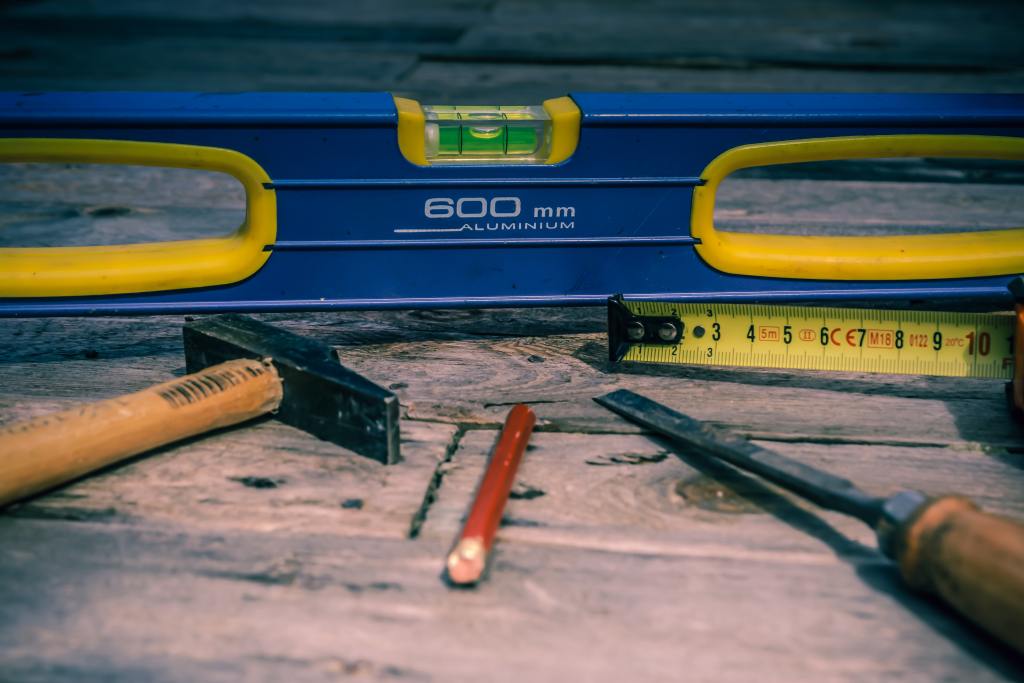 Tools clustered closely, including a blue and yellow colored level, a tape measure, a red pencil, and a ballpeen hammer.