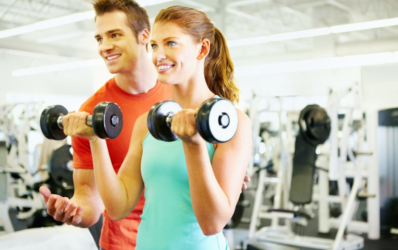 A person doing biceps curls with a trainer. 