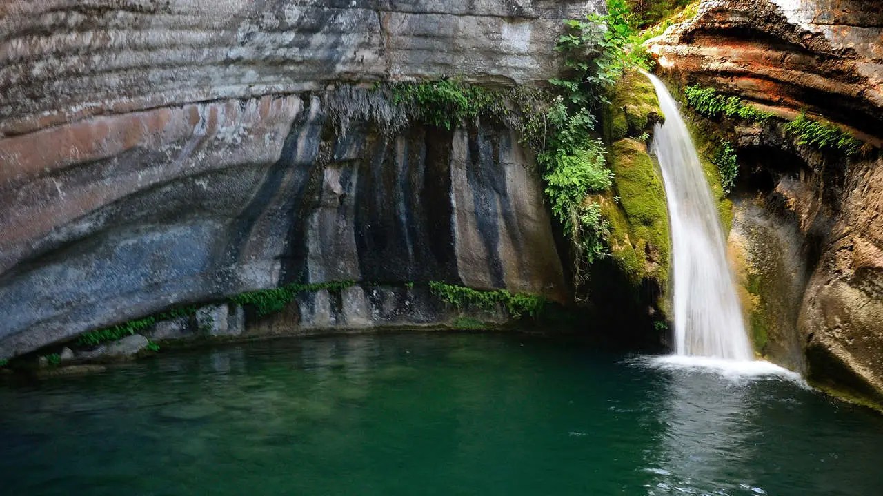 Cascada y poza natural del Toll de l’Olla en Farena, aguas verdes rodeadas de roca y vegetación