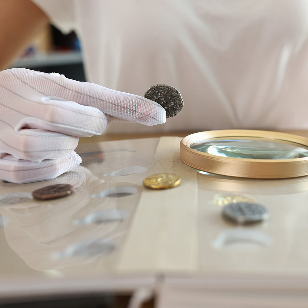 Collector examining coins using white gloves and a magnifying glass