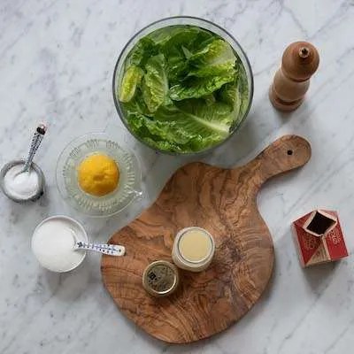 P&aring; billedet ses alle ingredienser til mormordressingen samt gr&oslash;n salat i en sk&aring;l med koldt vand