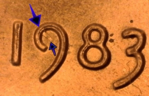 microscopic image of the 1983 date of a of a one cent penny worth money with arrows noting the struck through error on the 9 of the date